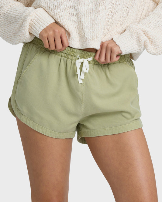 Avocado green shorts with elastic waistband and white drawstring tie, worn with cream ribbed sweater.