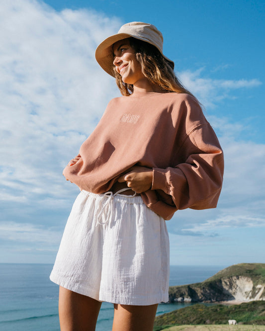 Woman wearing white woven shorts with drawstring waist and a terracotta sweatshirt.
