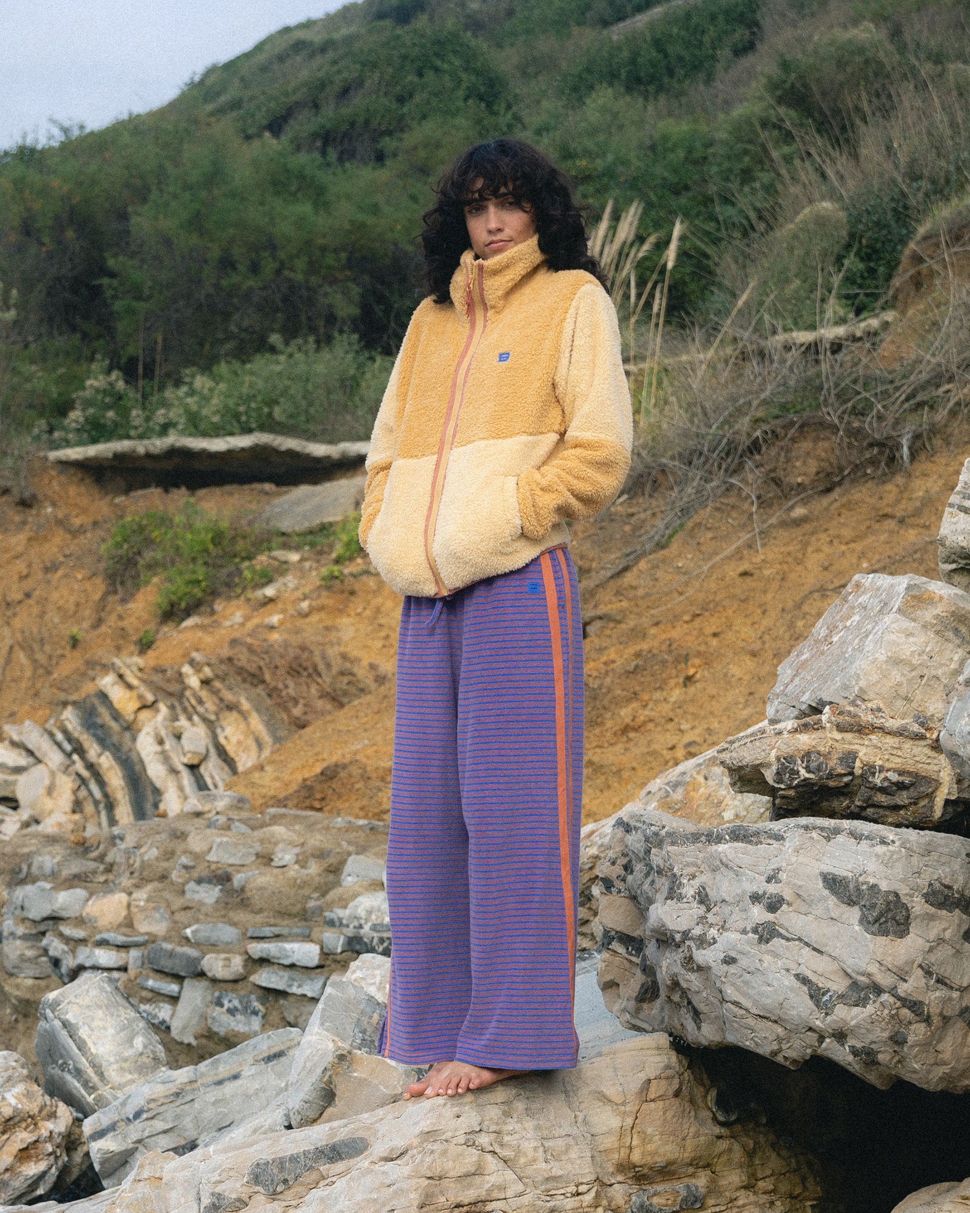 Iris terry pants with horizontal stripes worn with a yellow fleece jacket in an outdoor rocky setting.