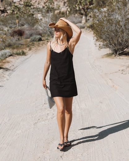 Black sleeveless slip dress with V-neckline worn on a dirt road.