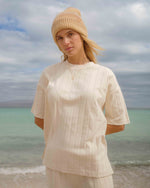 White ribbed short-sleeve top with vertical texture detail worn with a cream beanie by the ocean.