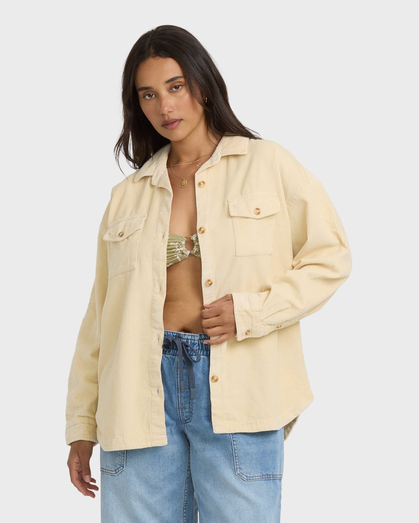 Cream-colored corduroy shacket with long sleeves, button front, and chest pockets worn open over a bikini top.