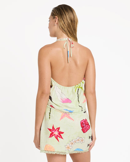 Woman wearing a lime green sleeveless woven tank dress with colorful floral and botanical print, halter neckline, and decorat