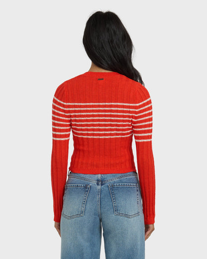 Red ribbed sweater with white horizontal stripes across the chest and sleeves, worn with blue jeans.