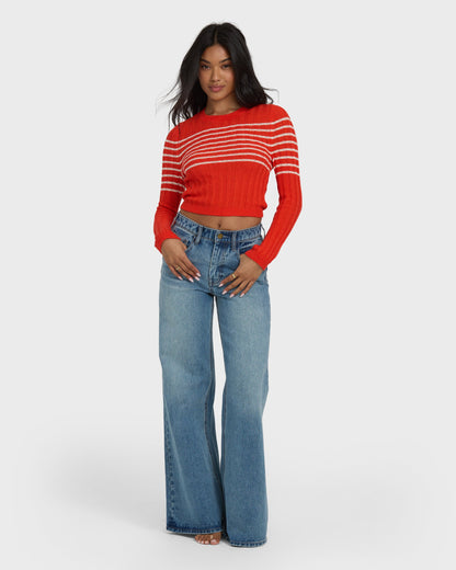 Red ribbed crop sweater with white horizontal stripes and long sleeves worn with light blue jeans.
