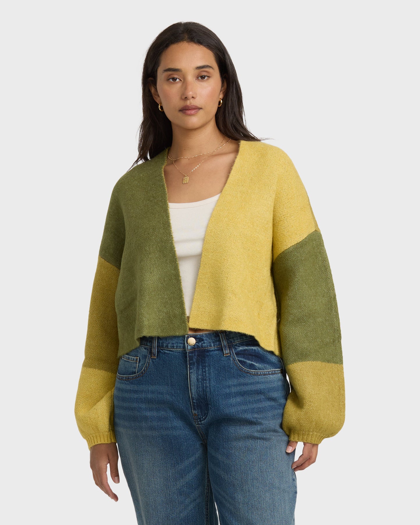 Woman wearing a color-block cardigan in green and yellow with long sleeves over a white top and blue jeans.
