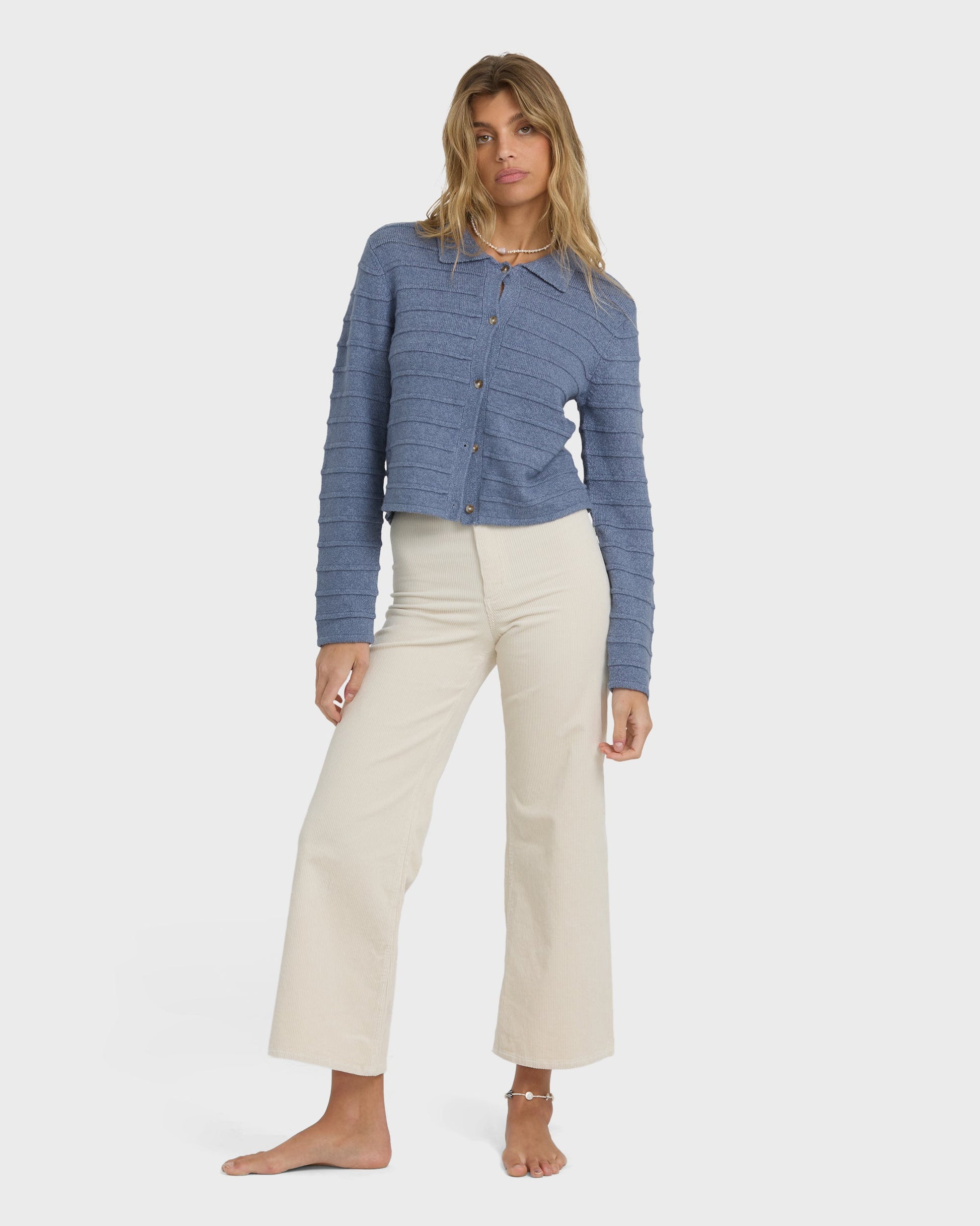 Stone blue quilted button-up sweater with long sleeves and collar, styled with cream pants.