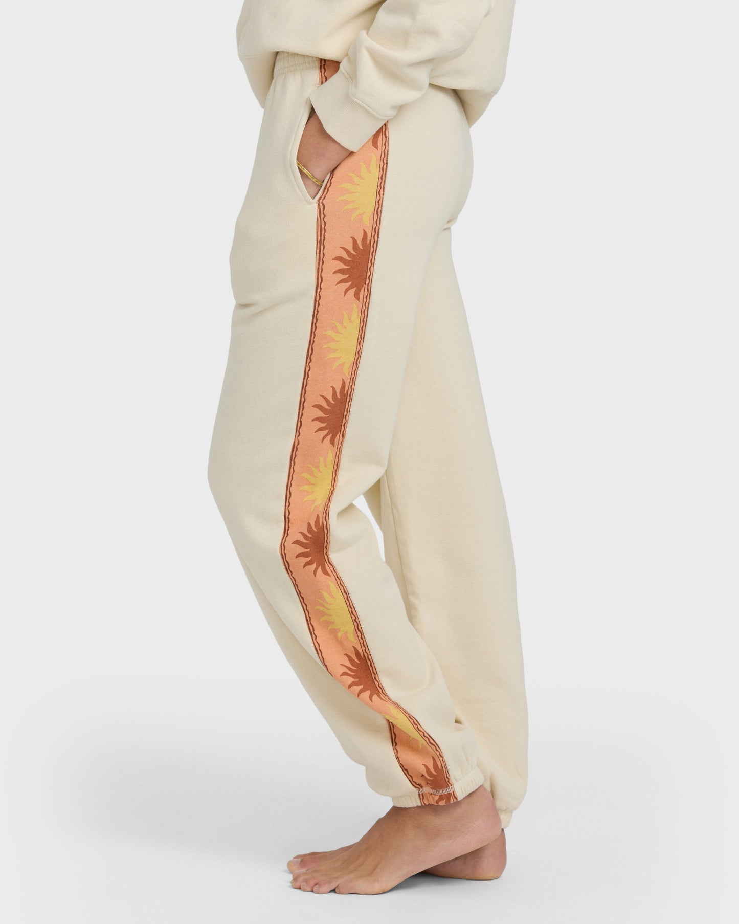 Cream joggers with coral and yellow sun-print stripe down the leg.