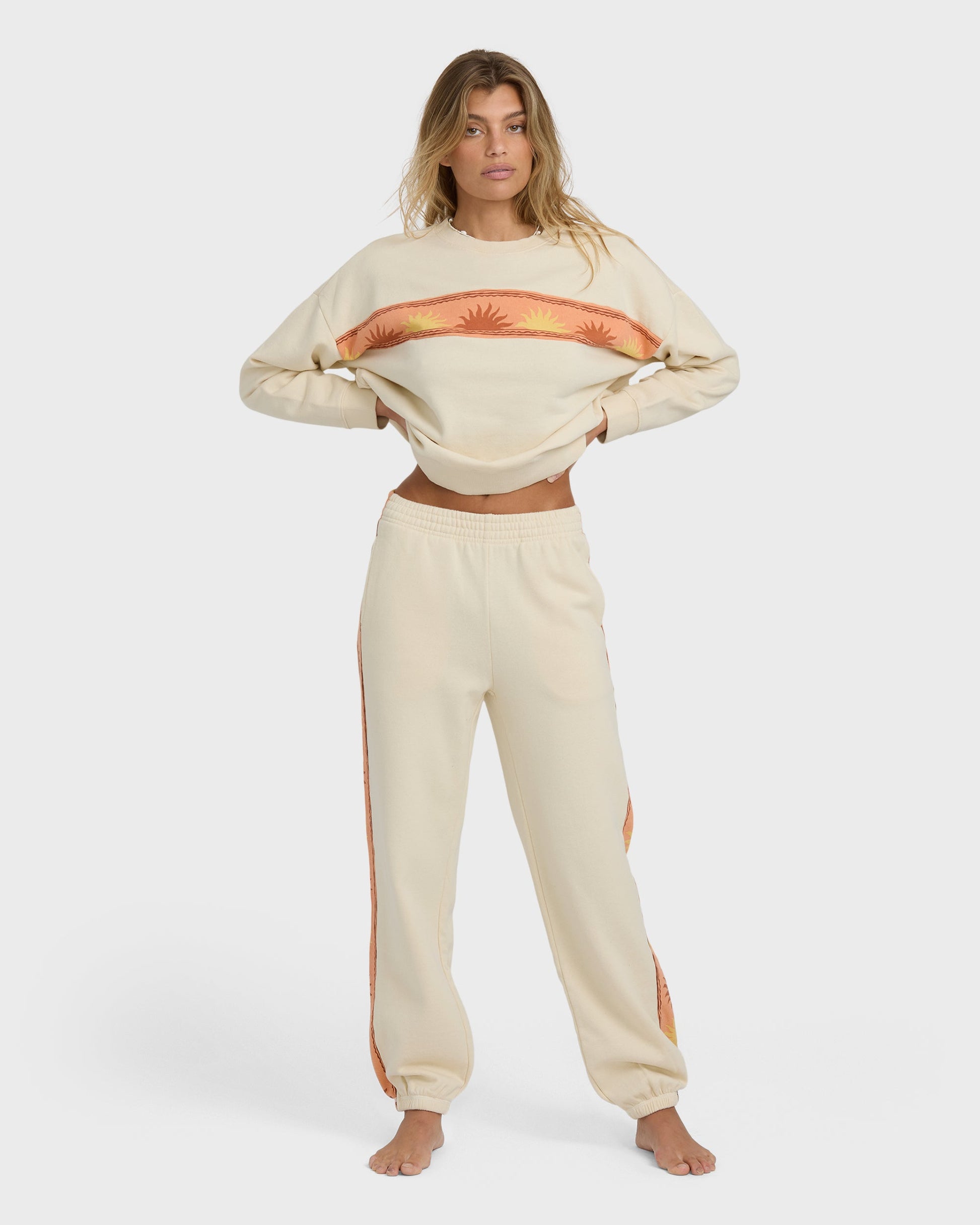 Cream-colored cropped sweatshirt and joggers set with orange sun stripe design on chest and side panels.