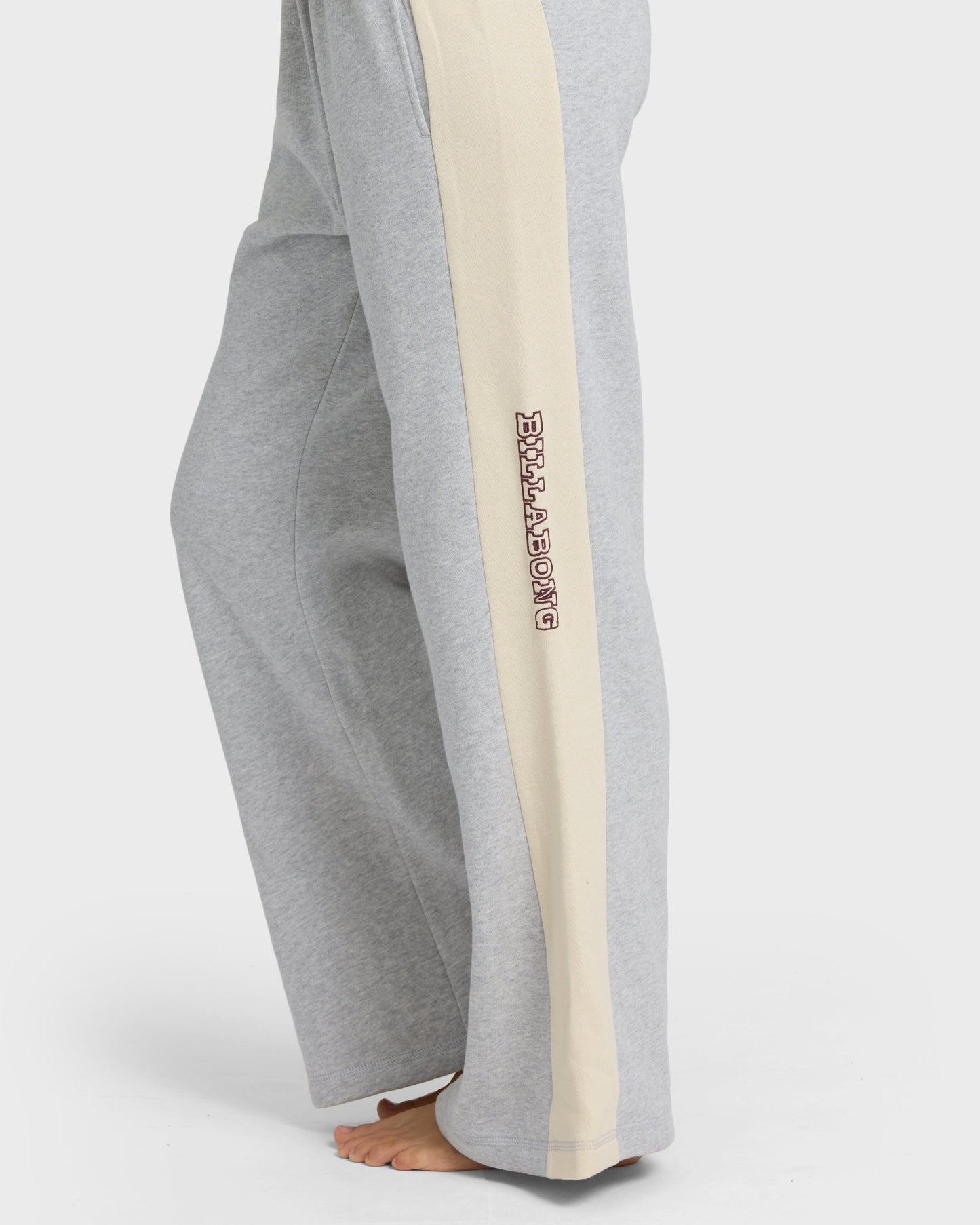 Heather grey sweatpants with cream side stripe and embroidered text on leg, shown on model from waist down.