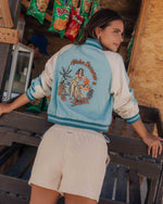 Misty blue and cream bomber jacket with "Aloha Dreams" graphic and hula girl illustration on back.