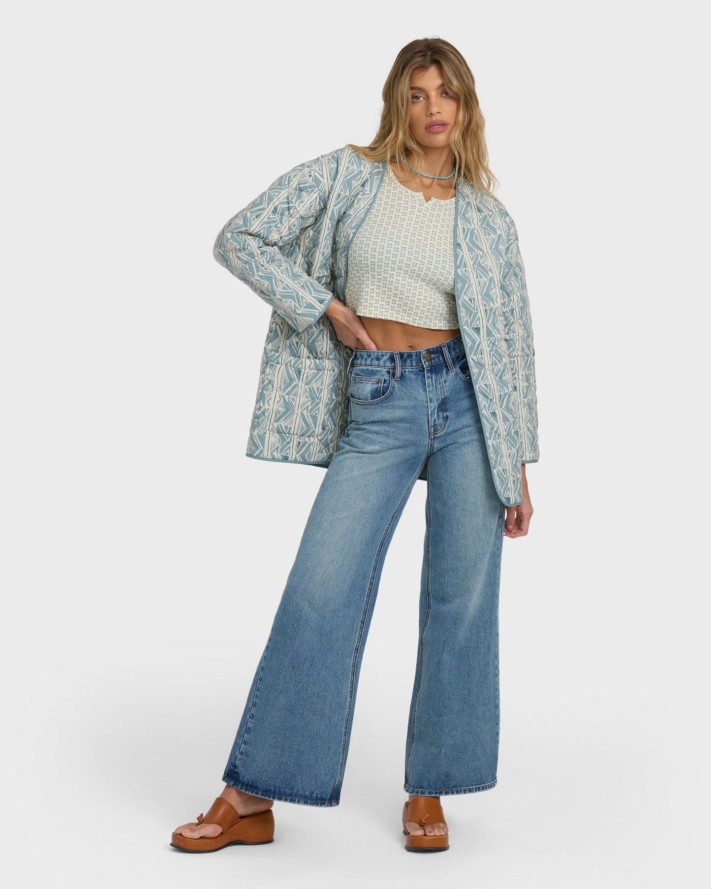 Mineral blue quilted jacket with geometric diamond pattern worn over a cream textured crop top and wide-leg jeans.