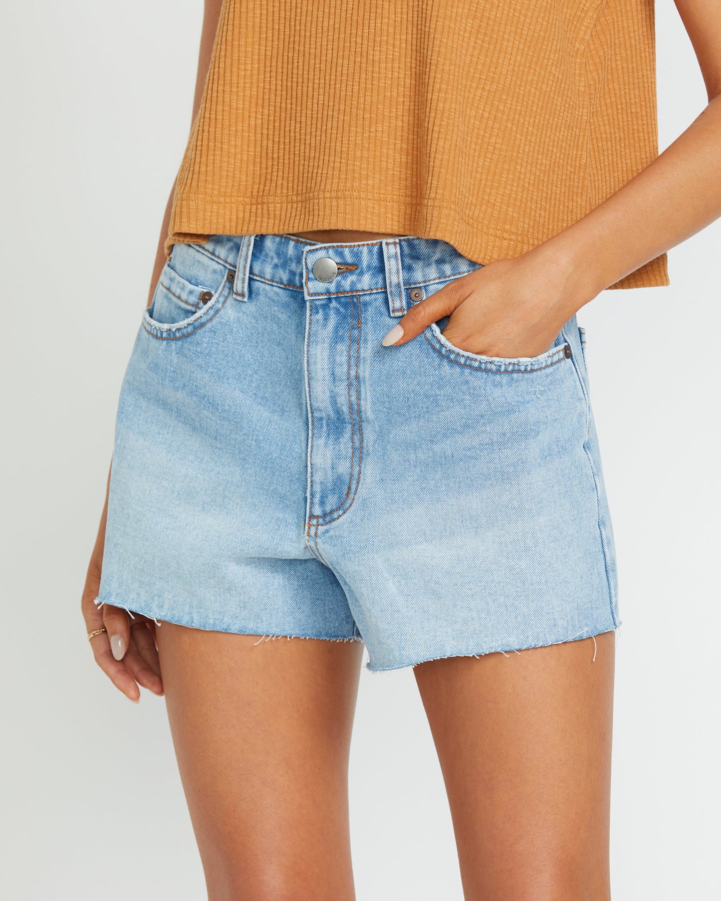Light blue denim shorts with frayed edges and a button fly, paired with an orange ribbed tank top.