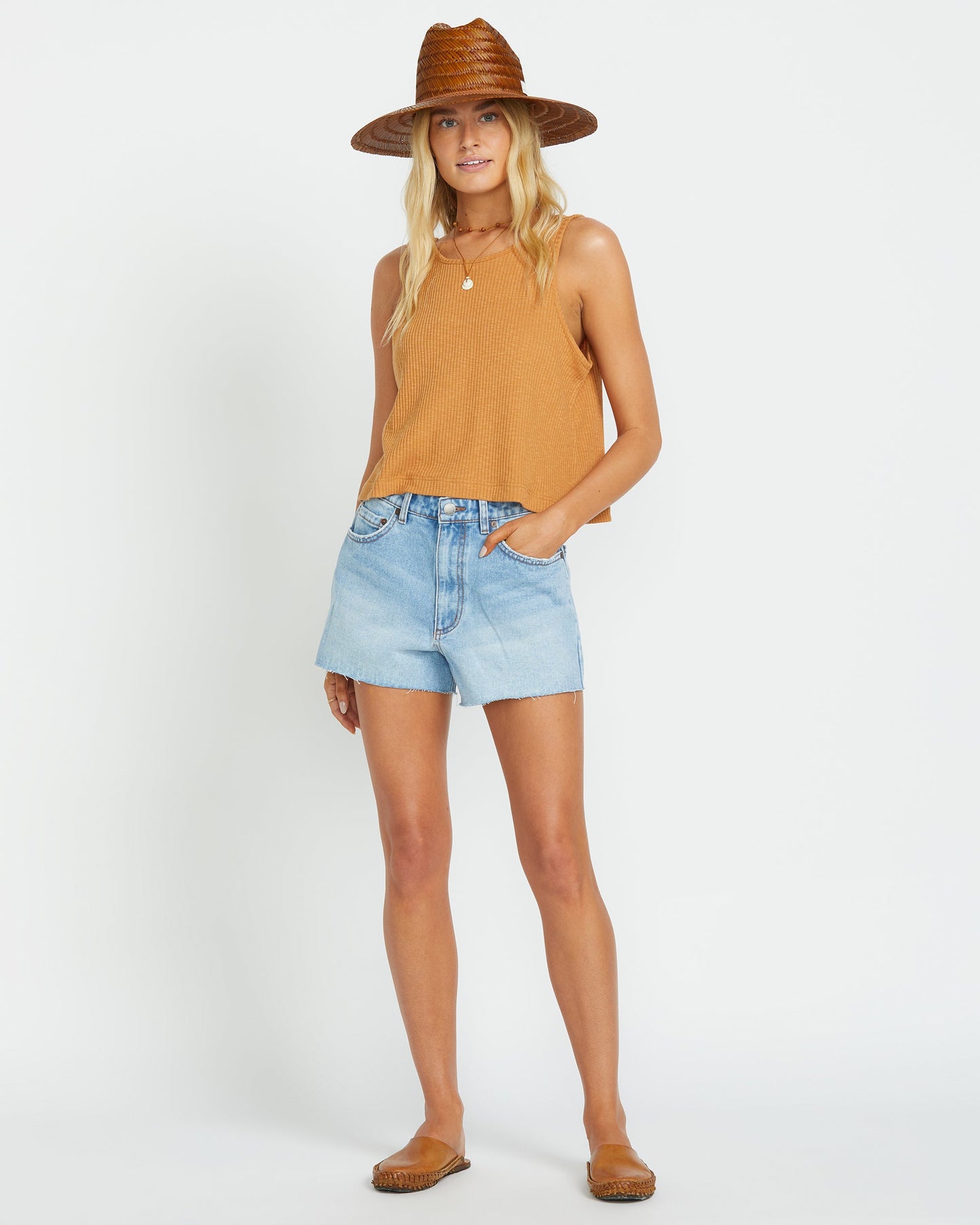Light wash denim shorts with raw hem, styled with yellow ribbed tank top and straw hat.