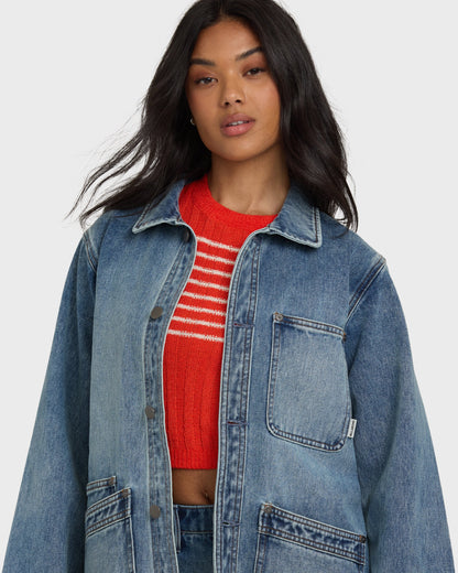 Blue denim chore coat with collar and chest pocket, worn over red striped sweater.