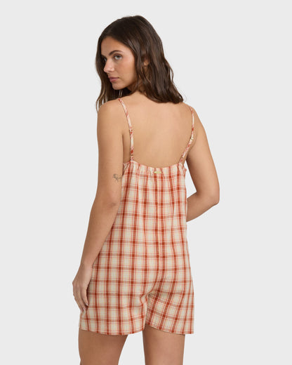 Woman wearing a rust and cream plaid sleeveless romper with thin shoulder straps and open back.