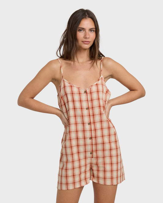 Woman wearing a rust and cream plaid romper with thin straps, button front, and shorts-style legs.
