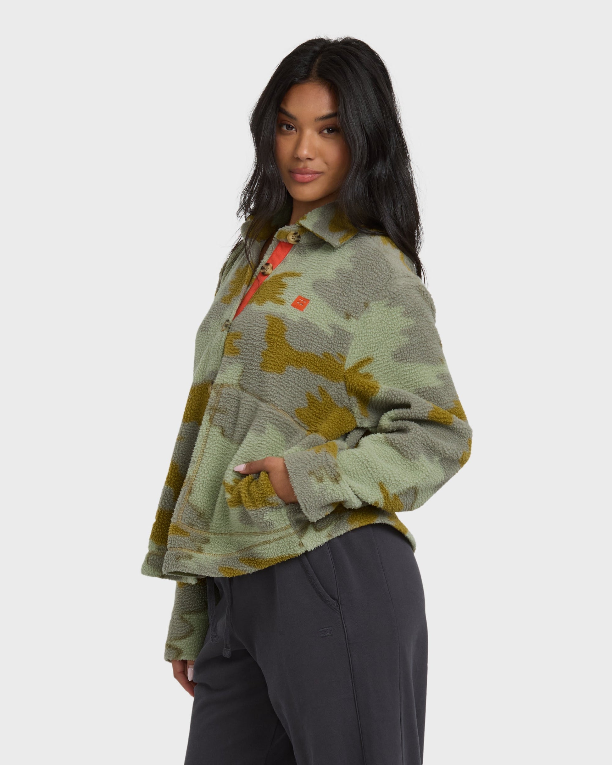 Camouflage sherpa shacket in sage and gold tones with button front and collar, paired with black pants.
