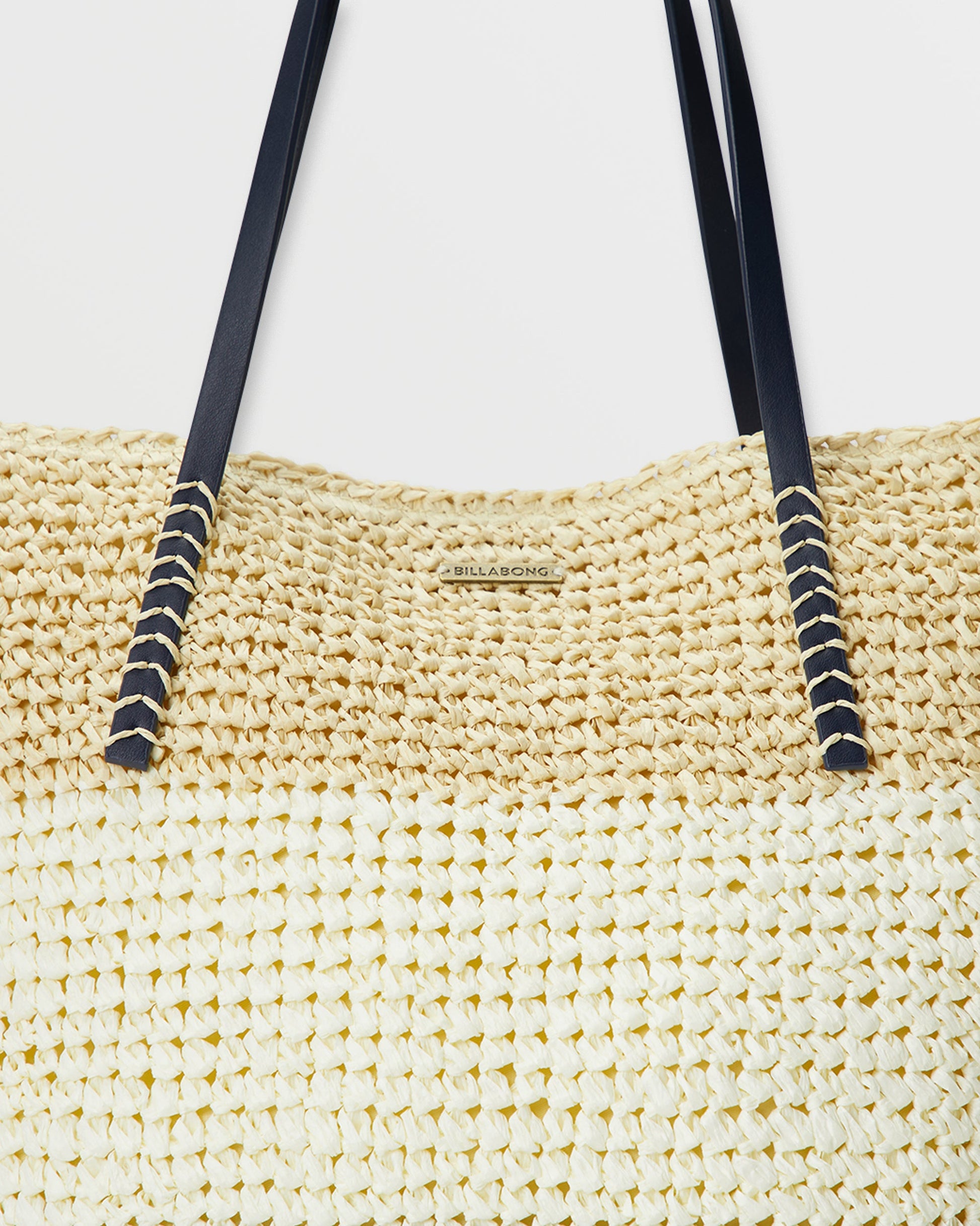 Woven straw tote bag in cream with navy shoulder straps and decorative rope detailing.