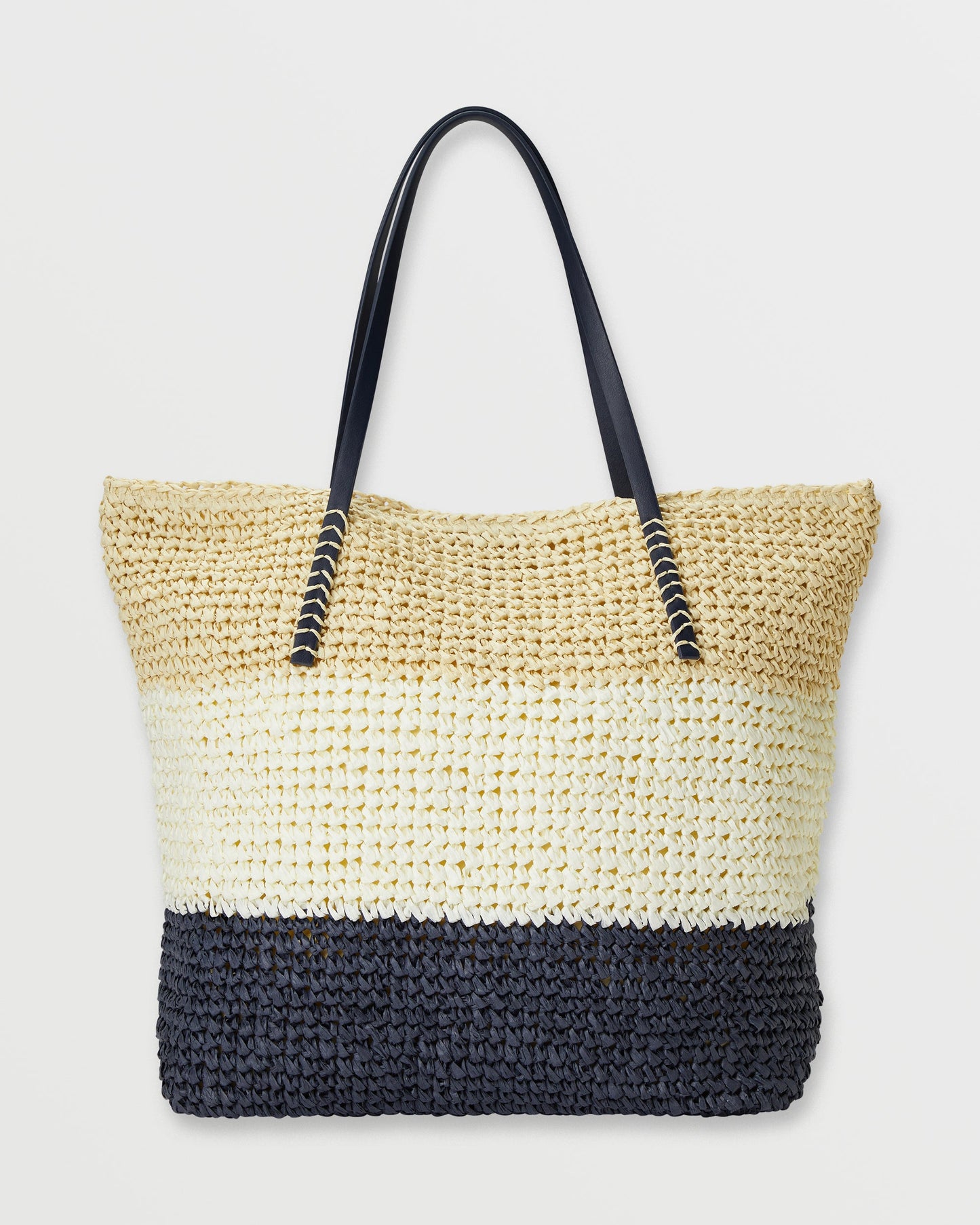 Woven straw tote bag with color-blocked design in natural, cream, and black sections, featuring black handles with metallic a
