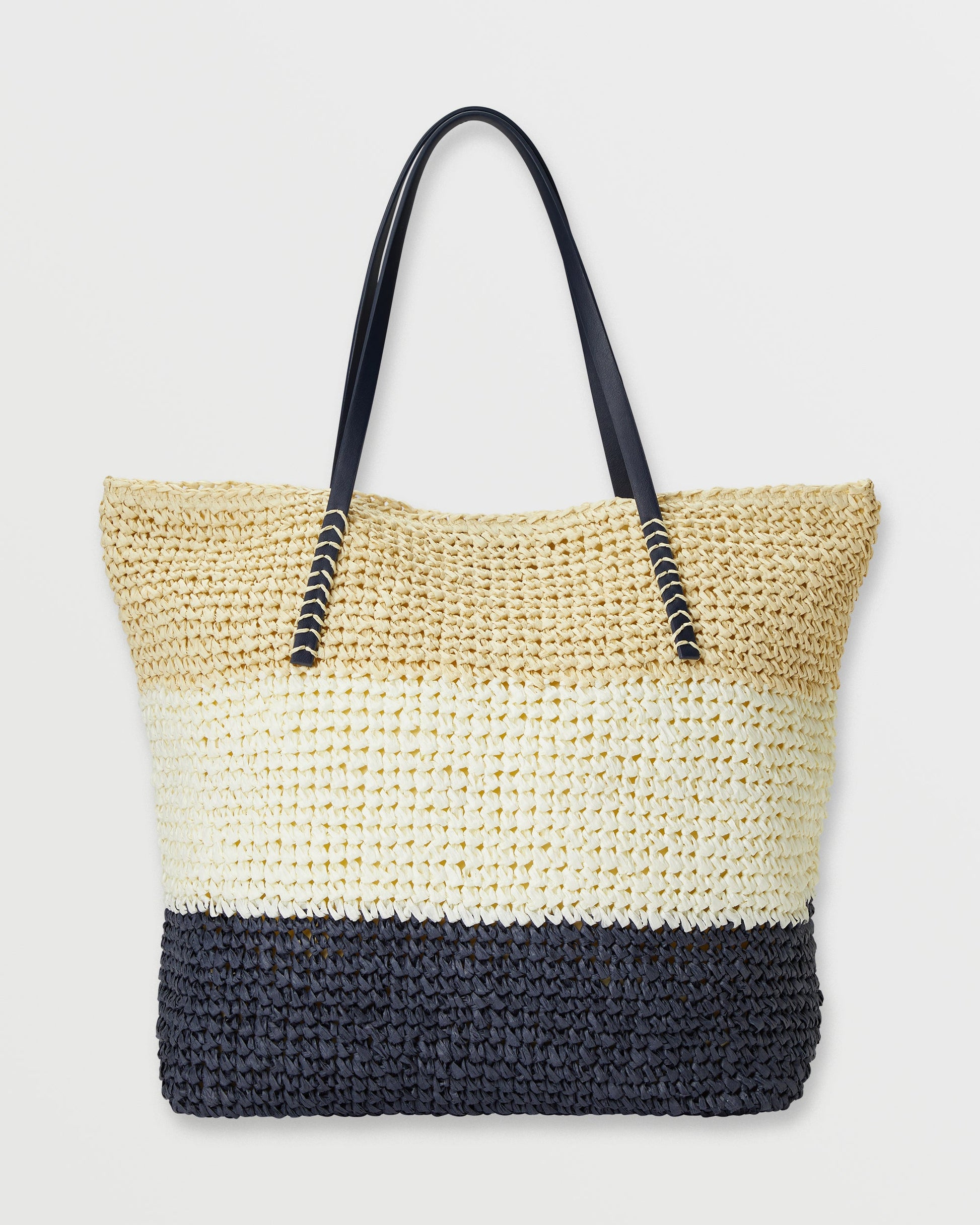 Woven straw tote bag with color-blocked design in natural, cream, and black sections, featuring black handles with metallic a