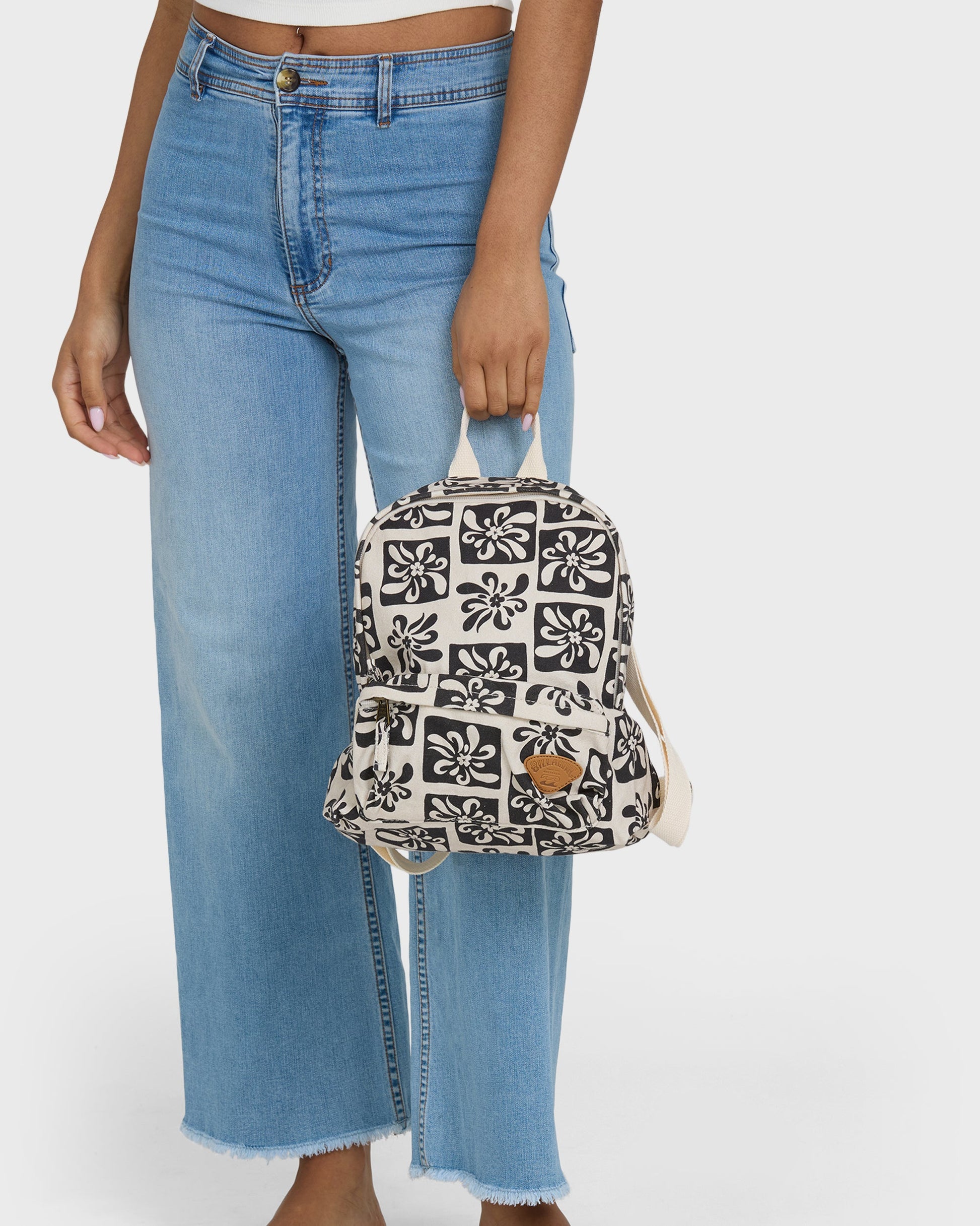 Black and white floral patterned mini backpack with tan leather accent held by person in blue jeans.