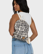 Black and cream backpack with geometric floral print, cream straps, worn on back by person in white tank and blue jeans.