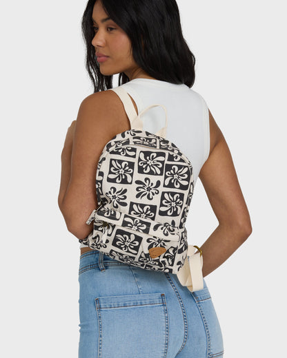 Black and cream backpack with geometric floral print, cream straps, worn on back by person in white tank and blue jeans.