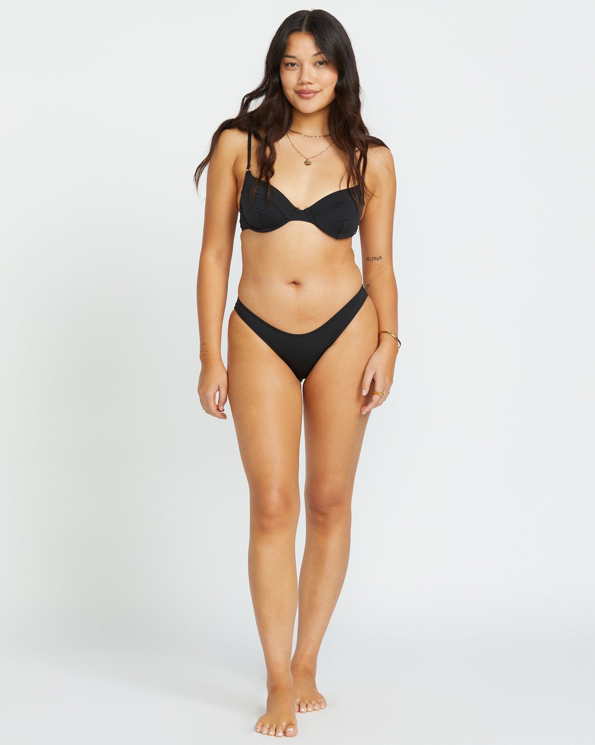 Black underwire bikini top with adjustable straps worn by model standing against white background.