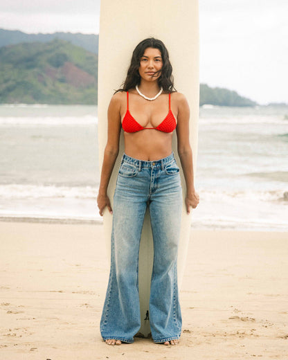 High-waist light blue denim flare pants with distressed details worn on beach.