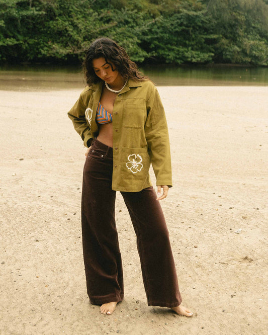 Brown corduroy wide-leg pants styled with a yellow-green jacket on a person standing on a beach.