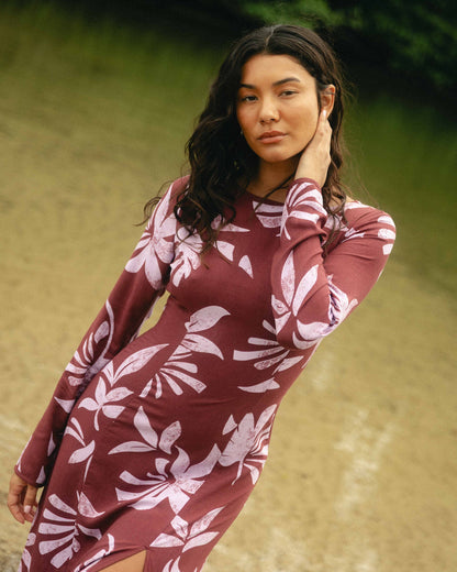 Burgundy maxi dress with white leaf print and long sleeves on model against blurred outdoor background.
