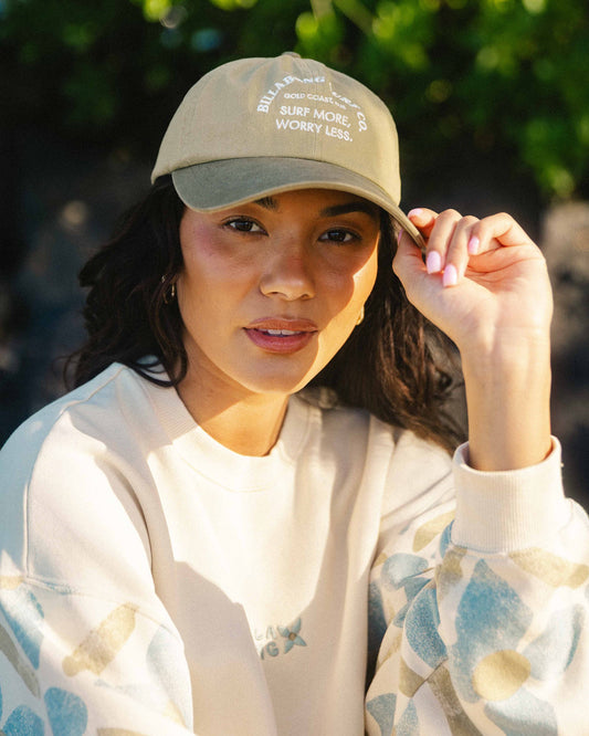Beige and gray dad cap with white embroidered text on crown, worn by person outdoors.
