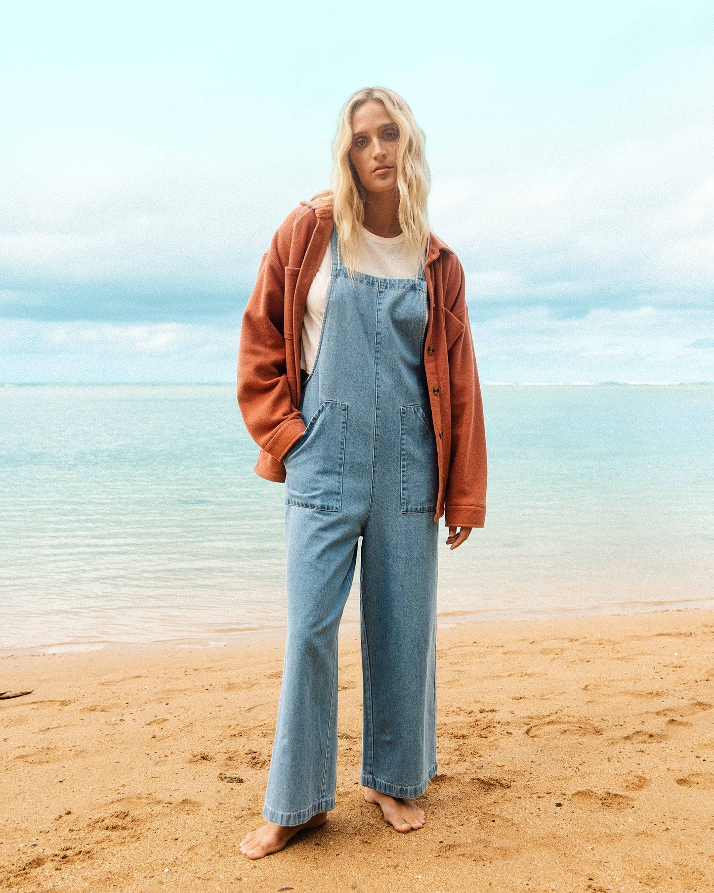 Light blue denim overall with adjustable straps, front pockets, and wide-leg cut worn over white shirt.