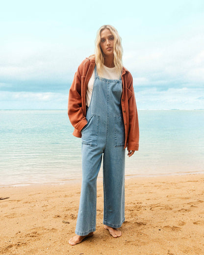 Light blue denim overall with adjustable straps, front pockets, and wide-leg cut worn over white shirt.