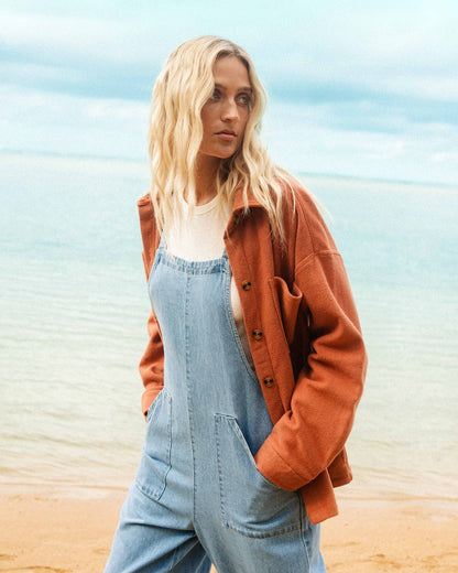 Light blue denim overall with bib pocket and adjustable straps, worn over white shirt.
