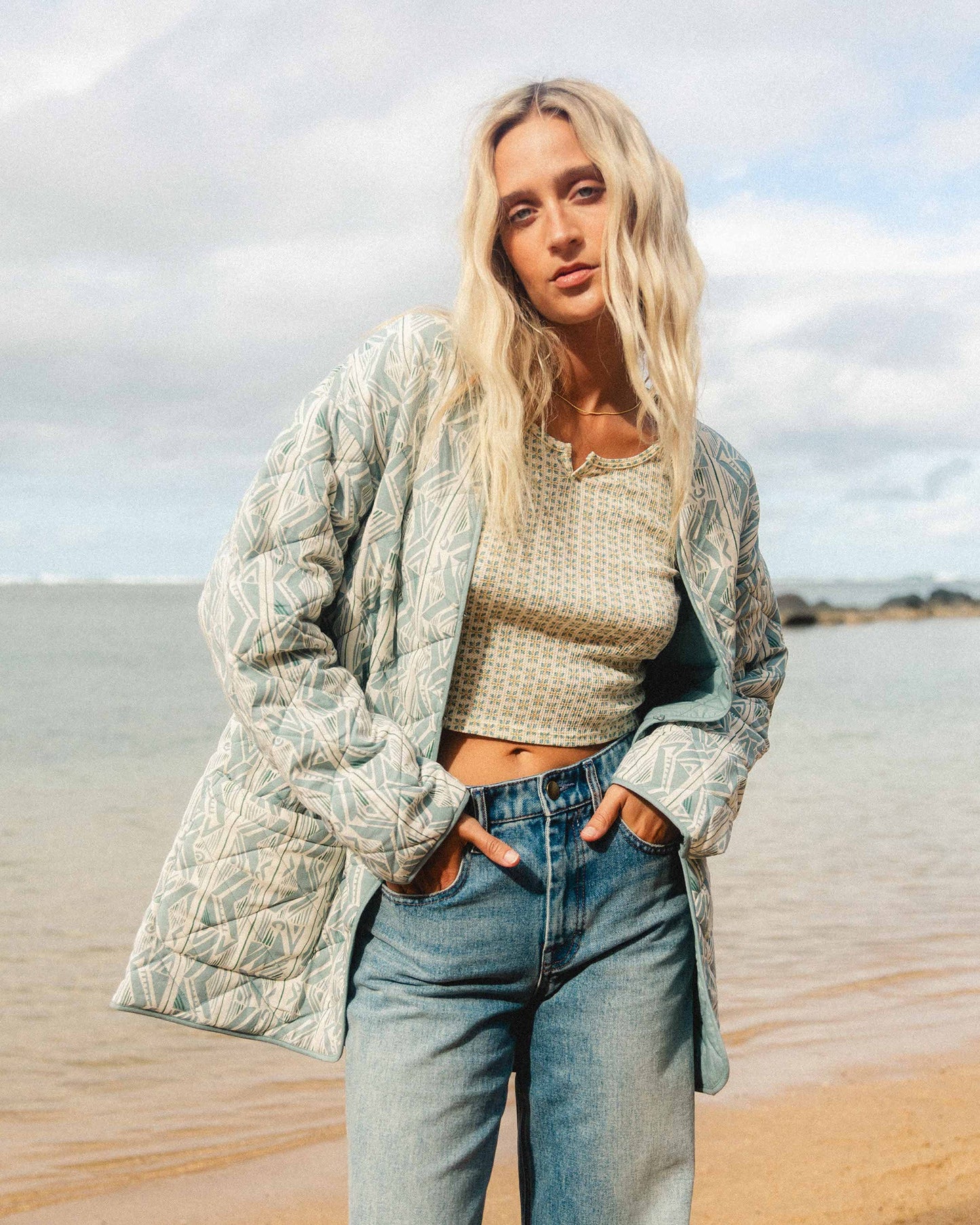 Mineral blue quilted jacket with leaf pattern worn over cream knit top and blue jeans.