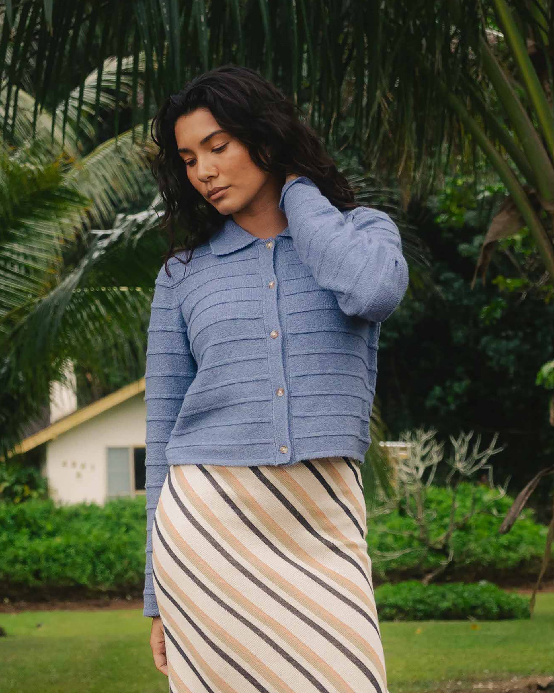 Stone blue quilted button-front sweater with horizontal stitching worn with striped skirt.