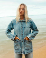 Medium-wash denim chore coat with chest and front patch pockets, button front, and rolled cuffs.