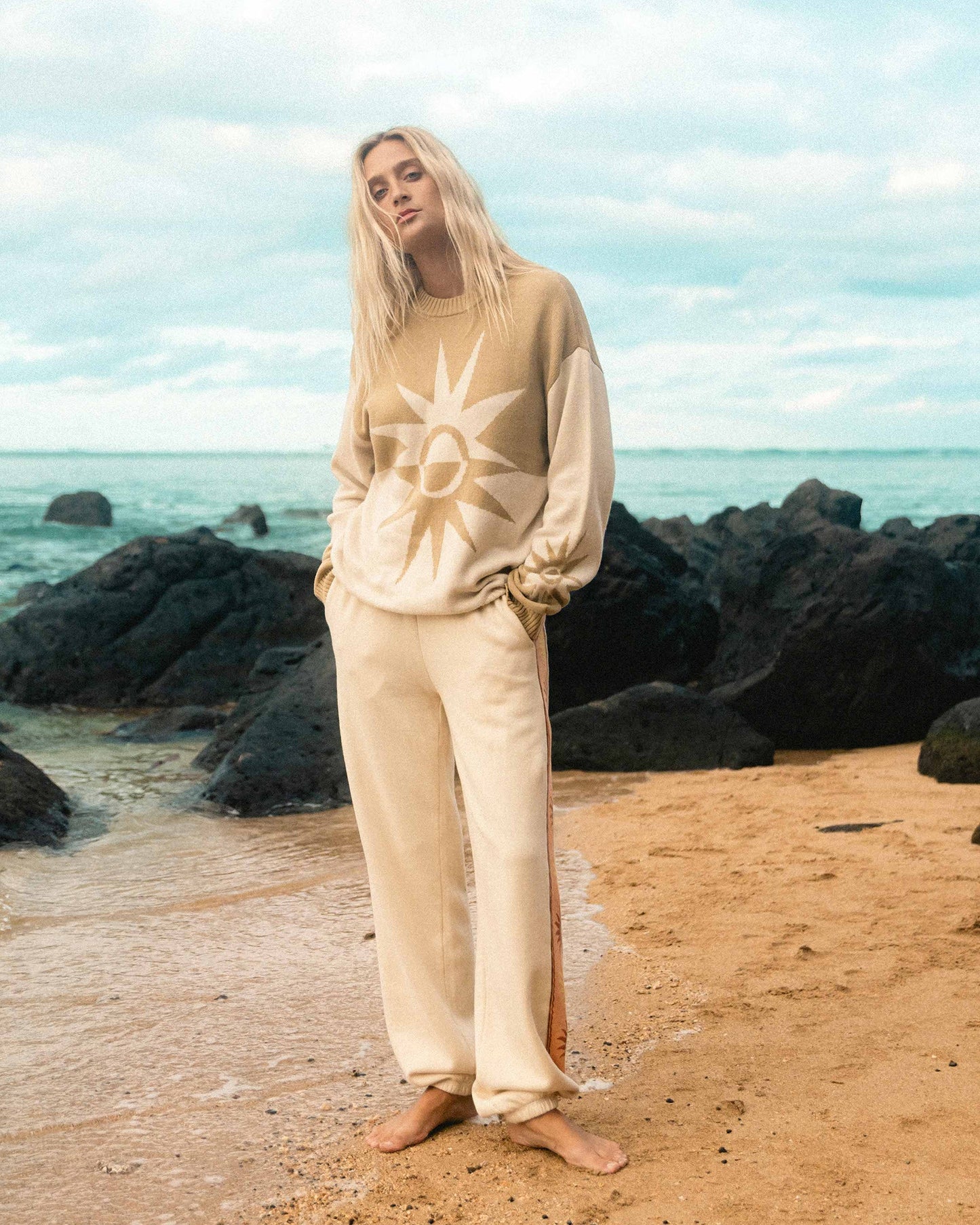 Cream-colored sweater with sun graphic on chest, worn with matching pants.