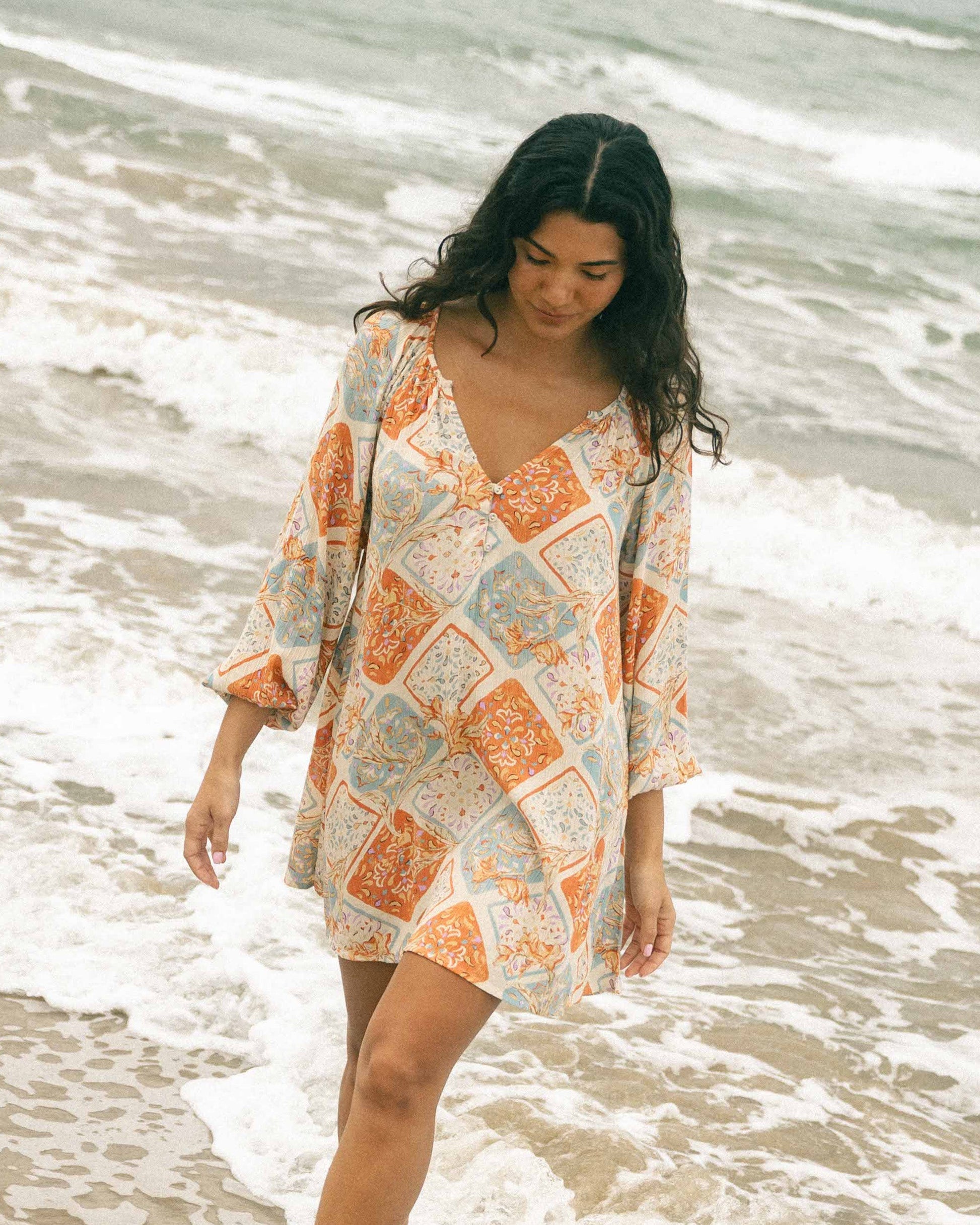 White mini dress with orange and blue patchwork floral print and three-quarter sleeves, shown on model at beach.