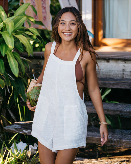 Woman wearing white sleeveless romper with square neckline, standing outdoors among tropical plants.