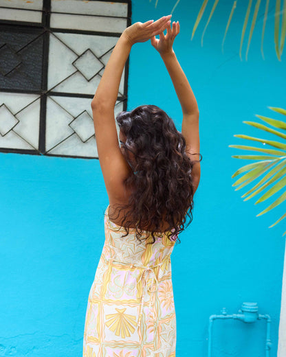 Woman wearing lilac midi dress with yellow and white geometric print, photographed from behind against blue wall.