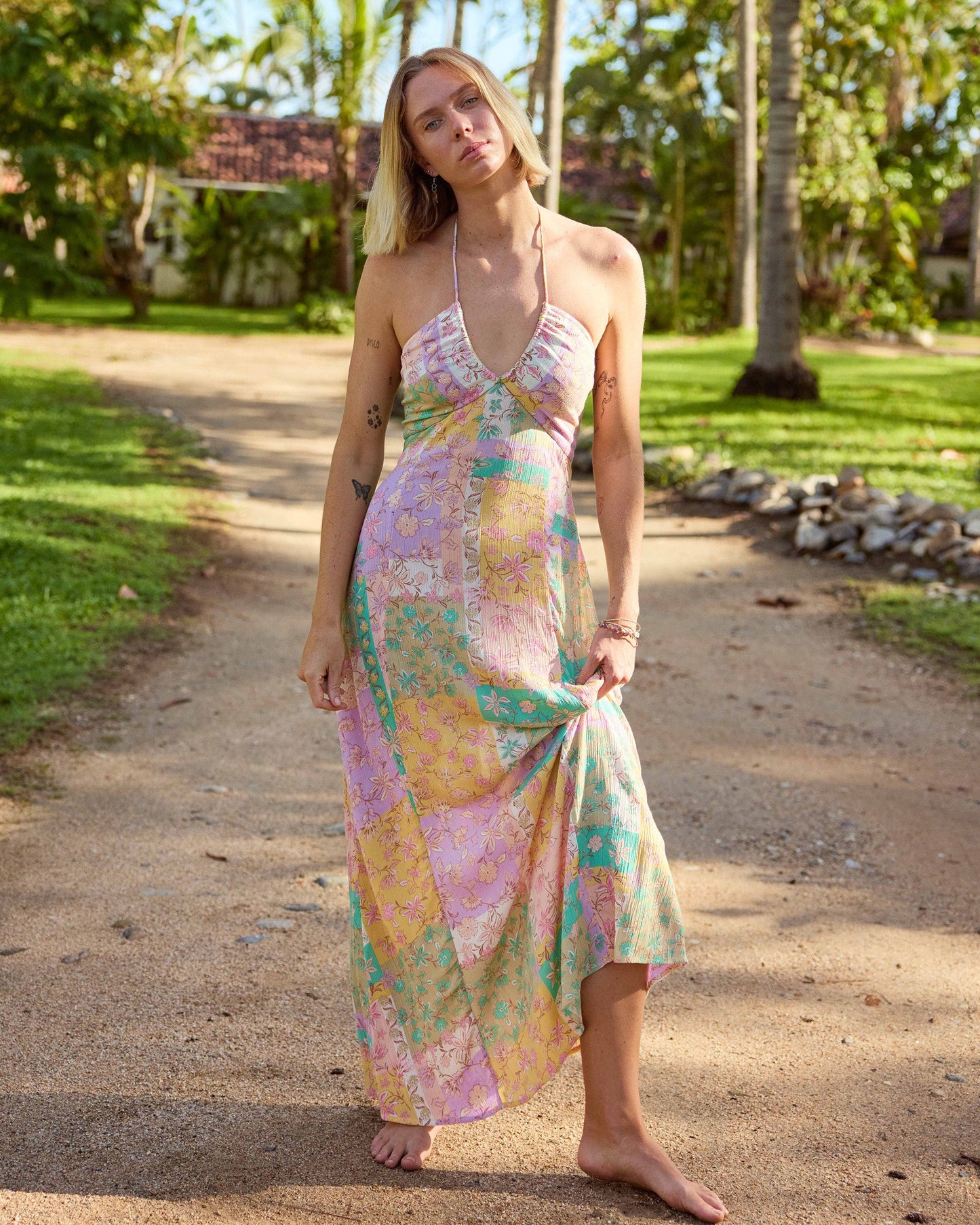 Woman wearing violet maxi dress with colorful floral print, halter neckline, and asymmetrical hem.