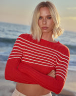 Red sweater with white horizontal stripes across the chest and sleeves, worn with arms crossed.