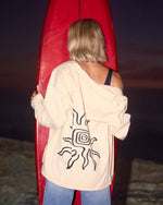 Antique white shacket with abstract line graphic on back, worn open over blue jeans.