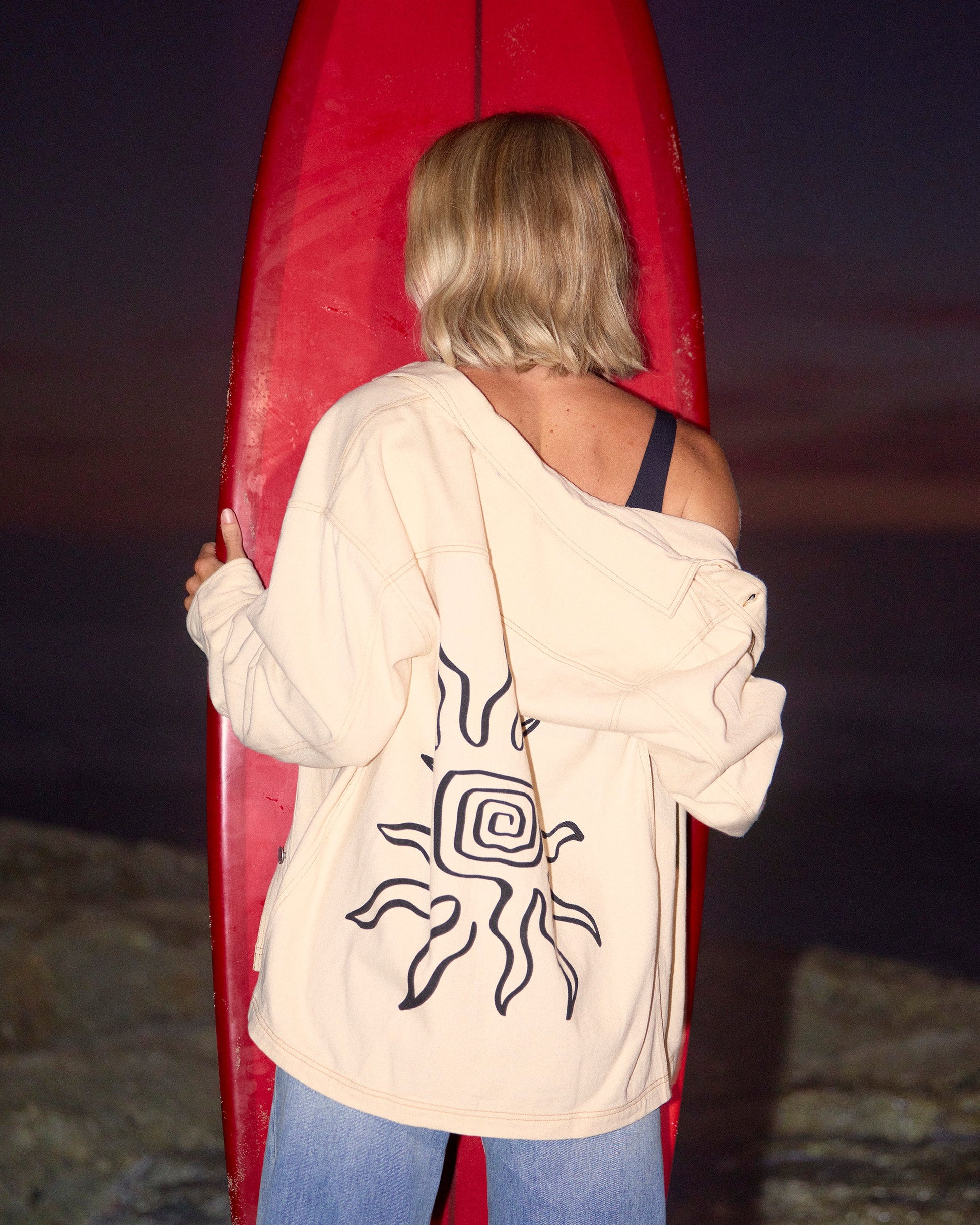 Antique white shacket with abstract line graphic on back, worn open over blue jeans.