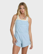 Light blue chambray sleeveless romper with front pocket and adjustable straps worn by model.