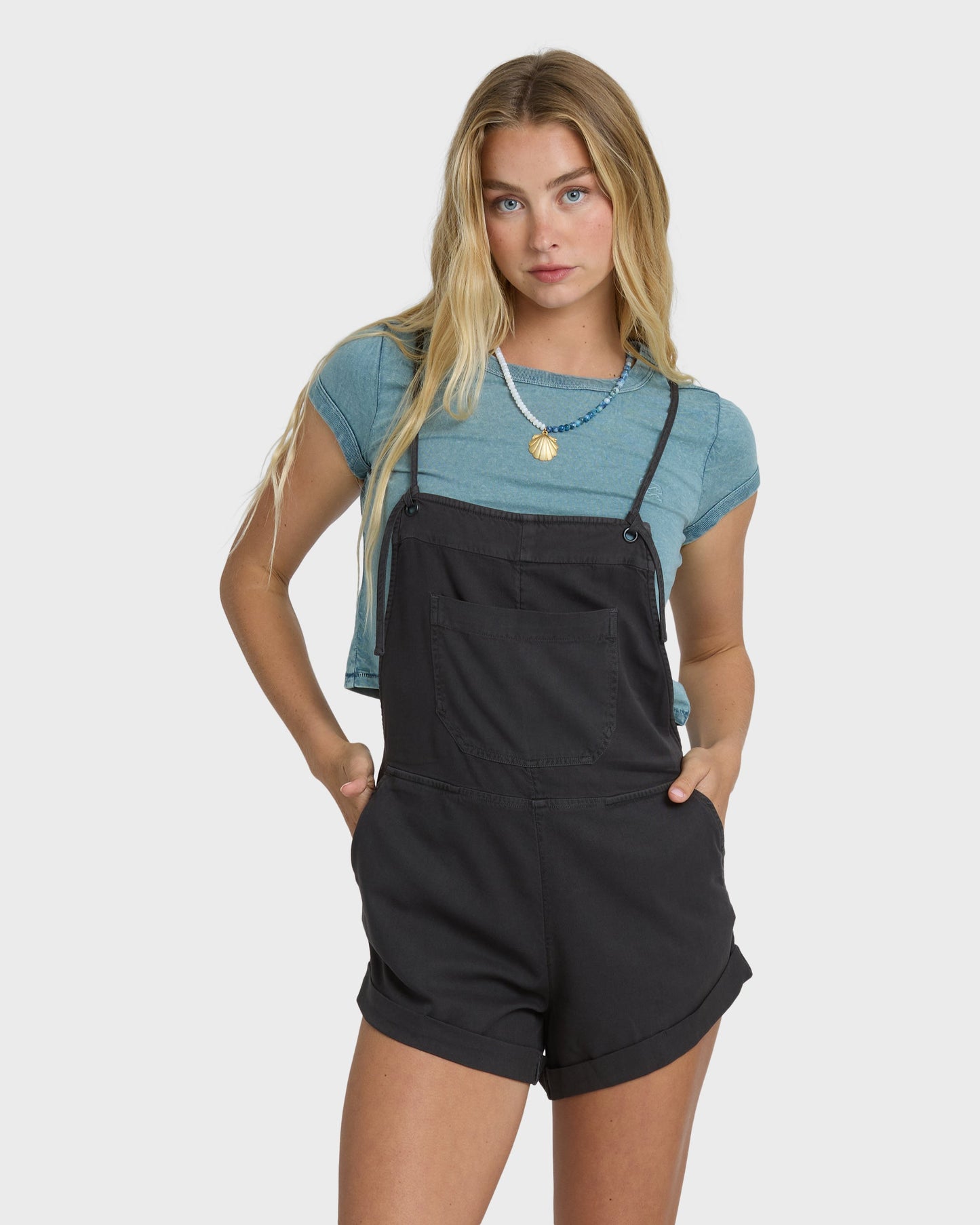 Off-black yarn-dyed overalls with adjustable straps and front pockets, worn over a blue t-shirt.