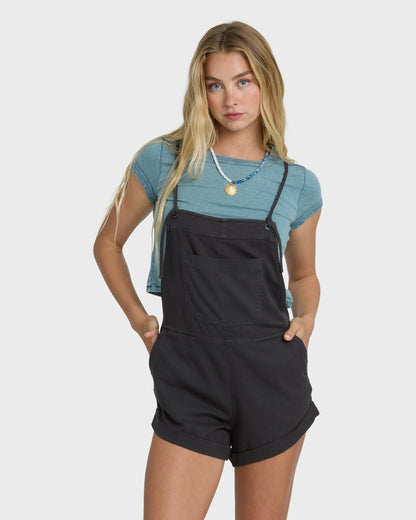 Off-black yarn-dyed overalls with adjustable straps and front pockets, worn over a blue t-shirt.